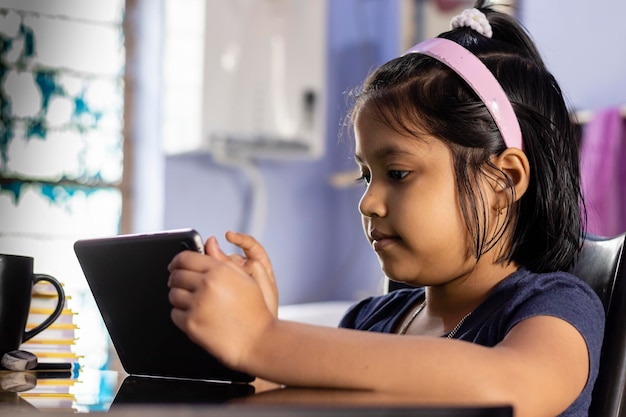 Una niña india linda estudiando en casa con una tableta