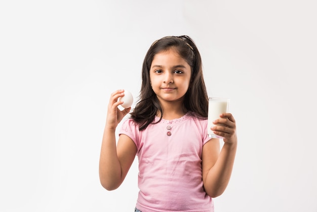 Niña india linda que sostiene un vaso de leche, huevo de gallina o manzana fresca. - concepto de alimentación saludable. Aislado en blanco