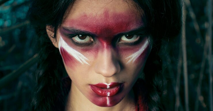 Foto niña india de piel roja con maquillaje rojo en el rostro posando en la hierba amarilla