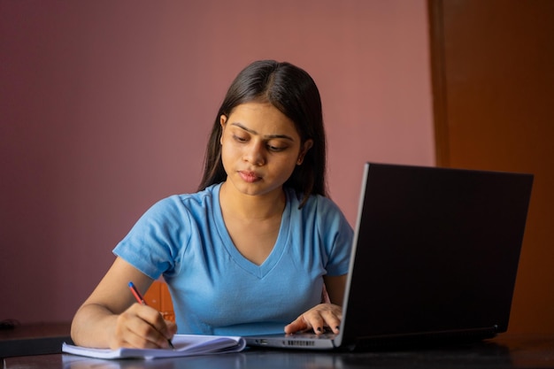 Niña india sentada en el escritorio estudiando o trabajando en una laptop tomando notas