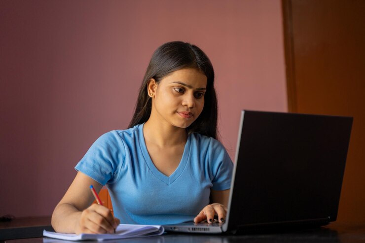 Niña india sentada en el escritorio estudiando o trabajando en una laptop tomando notas