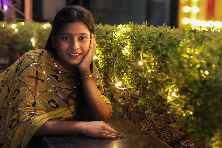 Niña india sonriendo frente a una planta decorada con luz para Diwali