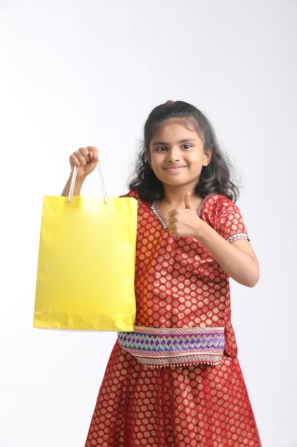 Niña india sosteniendo bolsa de compras y dando expresión sobre fondo blanco.