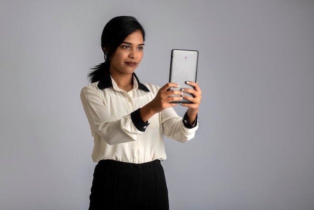 Niña india con un teléfono móvil o un teléfono inteligente en la pared gris