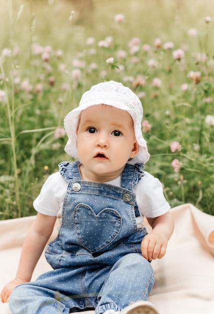 Una niña infante con una gorra blanca se sienta en el parque entre las flores.