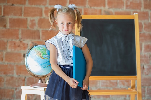 Niña infeliz en uniforme escolar con un libro en sus manos, concepto de regreso a la escuela