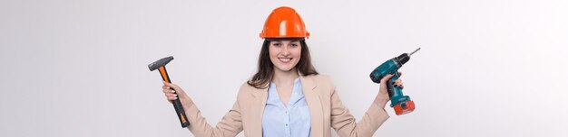 Niña ingeniera en un casco de construcción naranja con un destornillador y un martillo en un fondo blanco