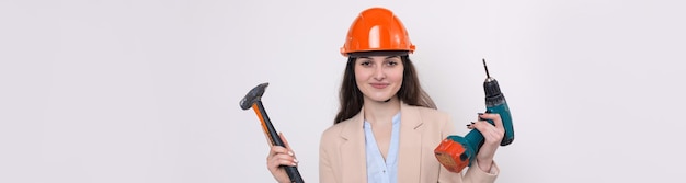 Niña ingeniera en un casco de construcción naranja con un destornillador y un martillo en un fondo blanco