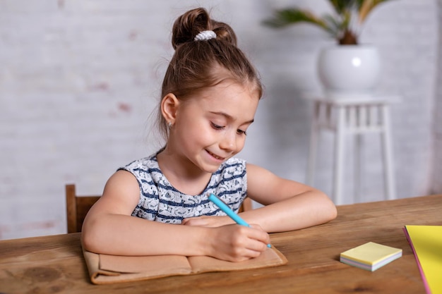 Una niña inspirada en la mesa dibuja con crayones o hace el trabajo a domicilio. Estudiar en la escuela primaria. Educación en casa