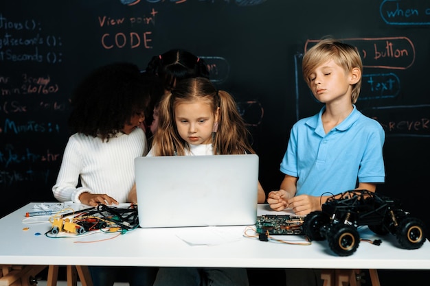 Niña inteligente con babero blanco aprendiendo tecnología robótica usando erudición de computadora portátil