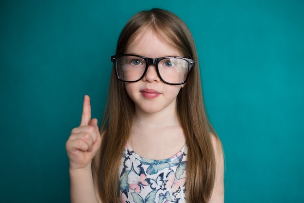 Foto niña inteligente con gafas apuntando sobre fondo verde concepto de educación y escuela