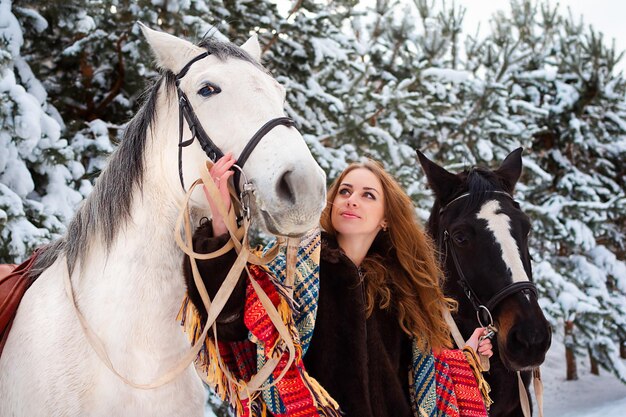 Una niña en invierno en el bosque se encuentra con caballos en la nieve.