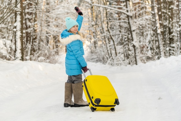 Una niña en invierno con botas de fieltro va con una maleta en un día de nieve helada