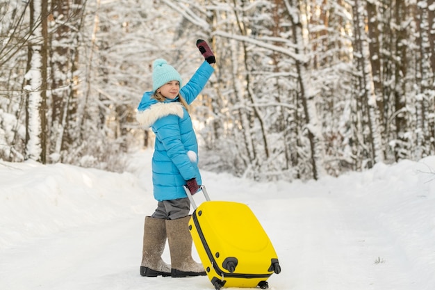 Una niña en invierno con botas de fieltro va con una maleta en un día de nieve helada.