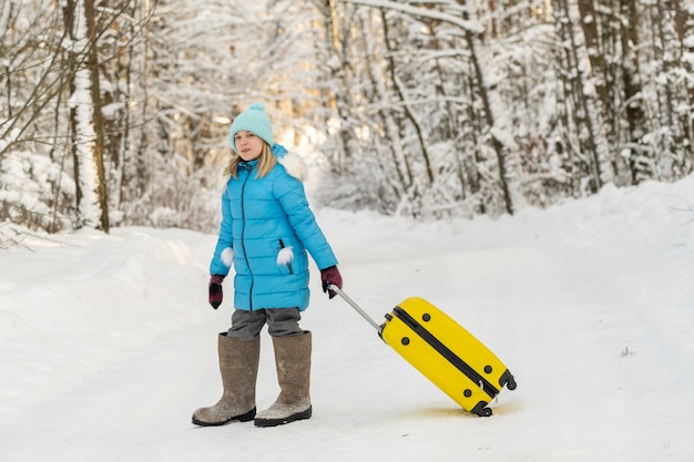 Una niña en invierno con botas de fieltro va con una maleta en un día de nieve helada
