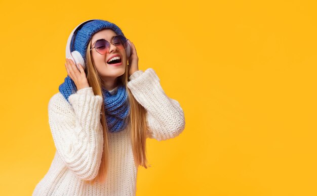 Niña de invierno emocional con auriculares inalámbricos y gafas de sol disfrutando de música de fondo rosa gratis