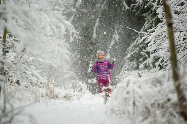 Una niña en invierno con ropa de color púrpura camina por un bosque cubierto de nieve