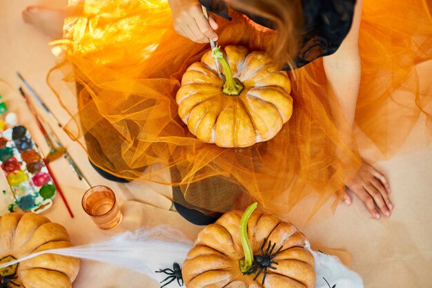 Niña irreconocible decorando una calabaza naranja, dibujando cara de Jack-O-Lantern para Halloween