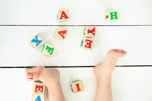 Niña irreconocible jugando con cubos abc en interiores. Letras en el piso. Fondo de la escuela