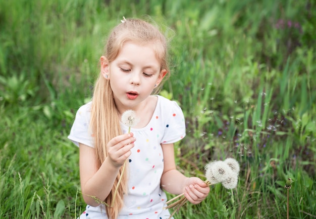 Niña en un jardín de primavera con dientes de león blancos en sus manos