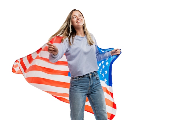 Una niña en jeans y una camiseta sin mangas azul sostiene una bandera estadounidense y se ríe. Celebrando el Día de la Independencia y el patriotismo. . Espacio para texto.