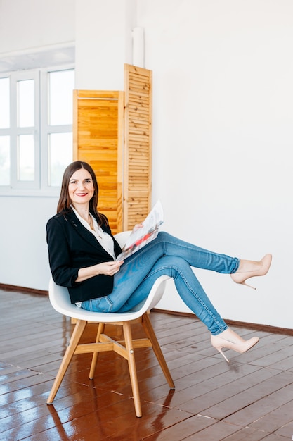 Una niña en jeans chaqueta ligera sienta la silla con una revista en sus manos, moda, lectura, entretenimiento, ocupación, editorial, freelance, hogar