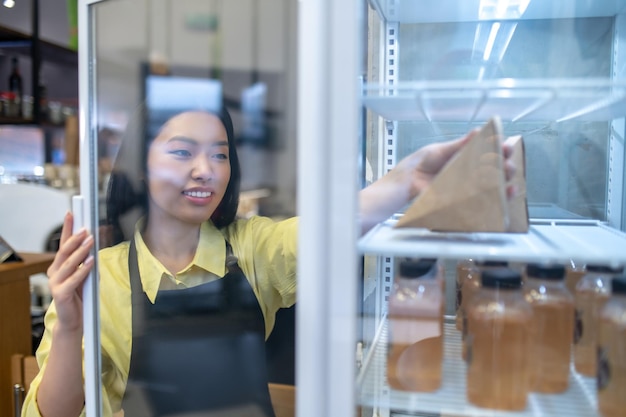 Niña joven en delantal tomando algo de comida de la nevera