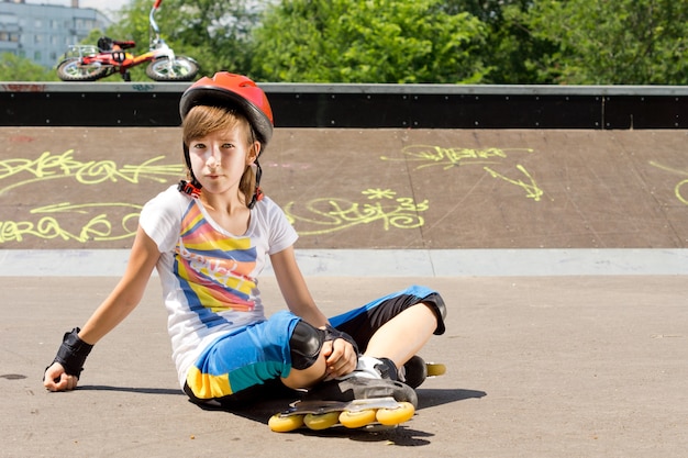 Niña joven, en, patines en línea, sentado, en, el, asfalto