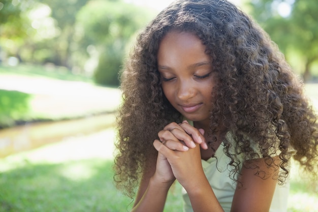 Niña joven, rezando, en el parque