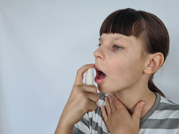 Foto niña joven rociando en la boca con spray contra el dolor en la garganta concepto