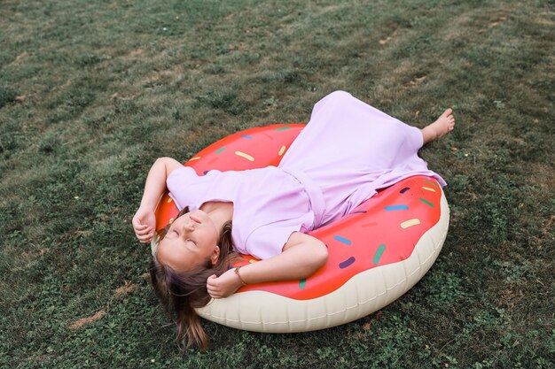 Una niña juega con un círculo inflable con un dout en el jardín en un caluroso día de verano.