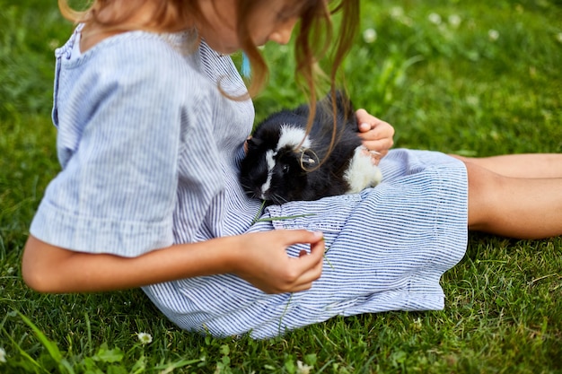 Una niña juega con el conejillo de Indias negro sentado al aire libre en verano