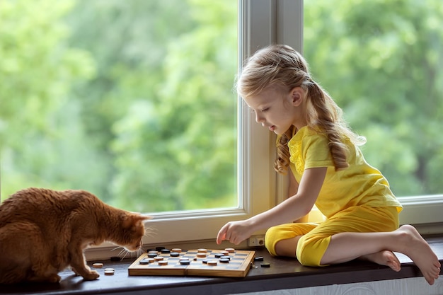 Niña juega a las damas con un gato Juegos intelectuales de mesa