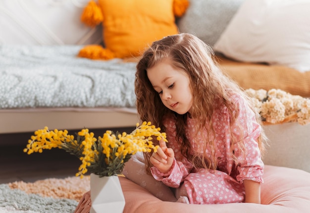 Niña juega con flores de mimosa en el suelo en el dormitorio infantil vintage