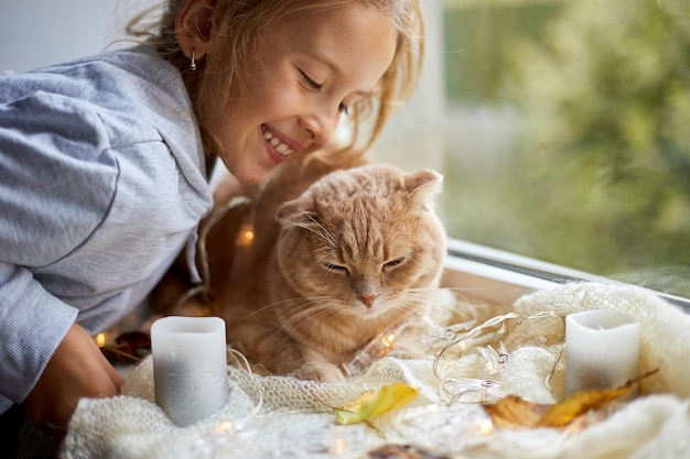 Foto niña juega con un gato acostado en el alféizar de la ventana en casa fin de semana perezoso de otoño con gato en casa