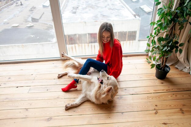 Niña juega con un golden retriever de raza de perro en casa en el piso mujer con mascota juntos yace en el piso