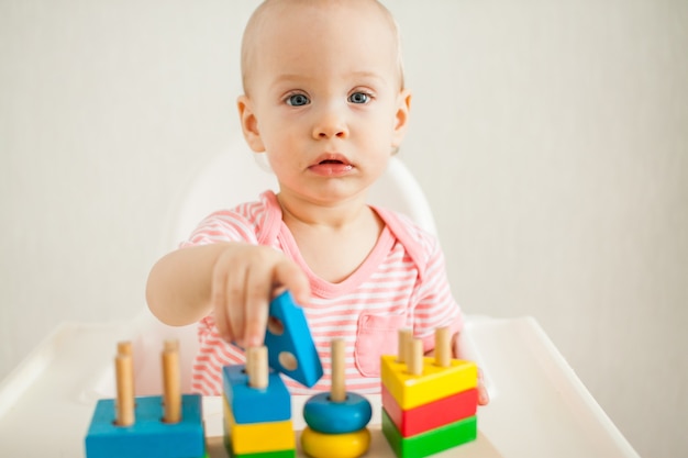 Foto la niña juega con un juguete educativo: una pirámide de madera multicolor. desarrollo de la motricidad fina y el pensamiento lógico. foto de alta calidad