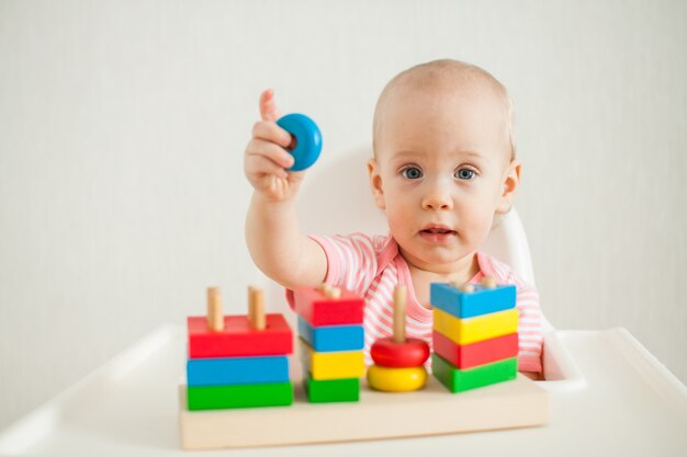 La niña juega con un juguete educativo: una pirámide de madera multicolor. Desarrollo de multa