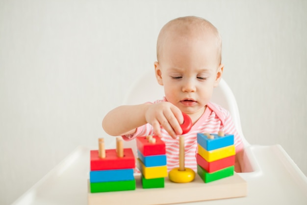 La niña juega con un juguete educativo: una pirámide de madera multicolor. Desarrollo de multa