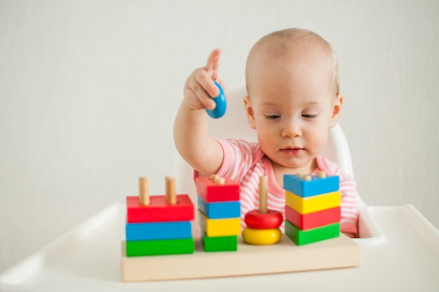 La niña juega con un juguete educativo: una pirámide de madera multicolor. Desarrollo de multa