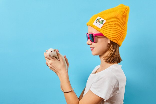niña juega con lindo toque de rata nariz pequeña le gustan los animales Ella usa sombrero amarillo casual y lentes