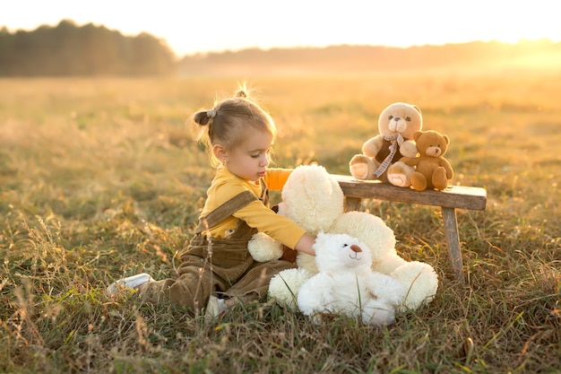 Una niña juega con osos de peluche en un campo al atardecer