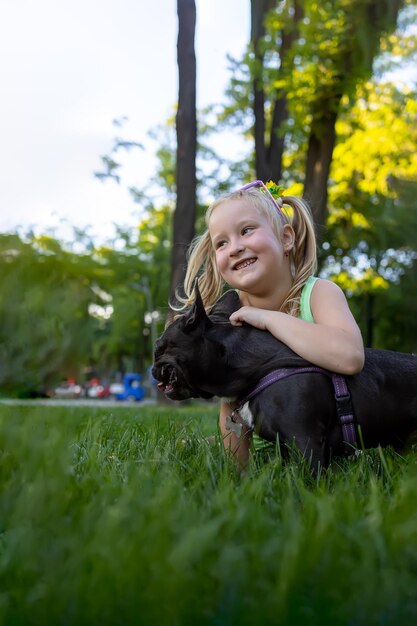 Una niña juega en el parque con un perro bulldog francés lo abraza y se ríe alegremente