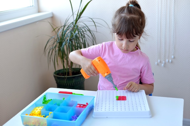 La niña juega el rompecabezas educativo infantil con un destornillador, un destornillador y shurukas con formas geométricas multicolores. concepto de desarrollo creativo para niños en edad preescolar.