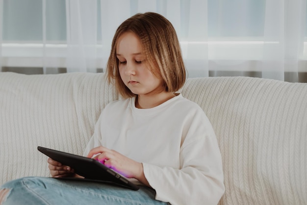 La niña juega en una tableta en el sofá