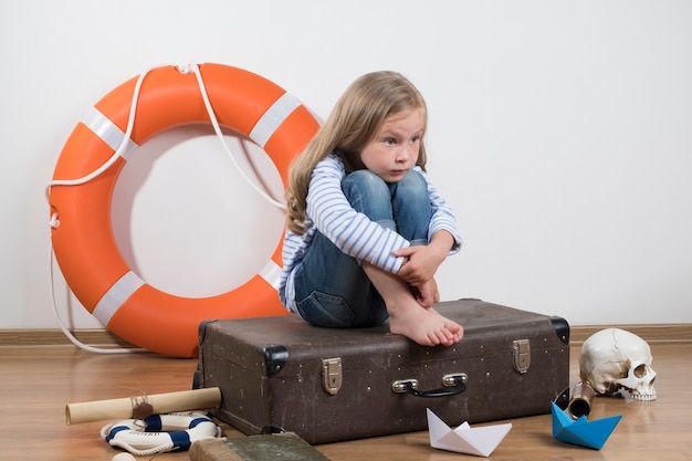 La niña juega en un viaje por mar Niña sentada en una maleta