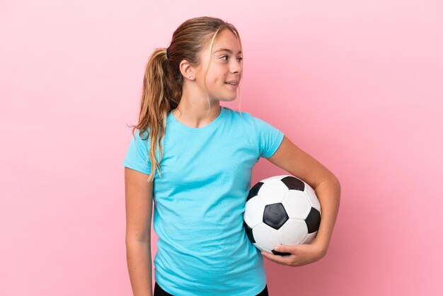 Niña de jugador de fútbol aislado sobre fondo rosa mirando de lado