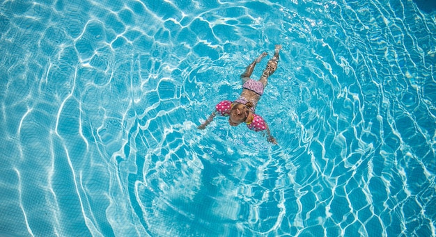 Niña jugando en el agua de la piscina al aire libre en vacaciones de verano Niño aprendiendo a nadar