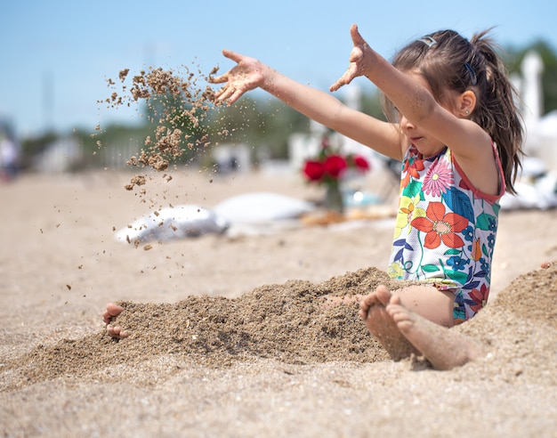 Niña jugando con arena en la playa. Un niño alegre. El concepto de vacaciones de verano.