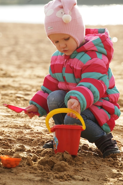 Niña jugando con arena en la playa de otoño